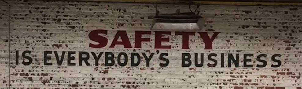 The message “Safety is everybody’s business” is painted on a brick wall.