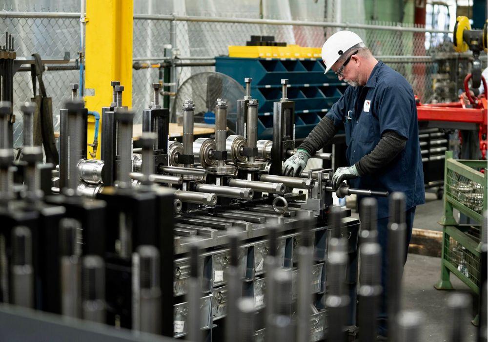 A manufacturing worker wearing a hard hat and safety glasses adjusts tooling on a roll forming machine inside CDH Custom Roll Form's production facility.