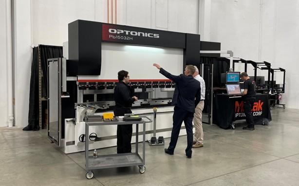 Three people stand in front of a press brake.