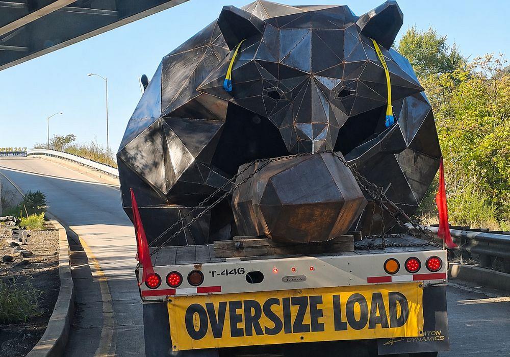 The large metal sculpture of a raccoon is affixed to a lowboy trailer.