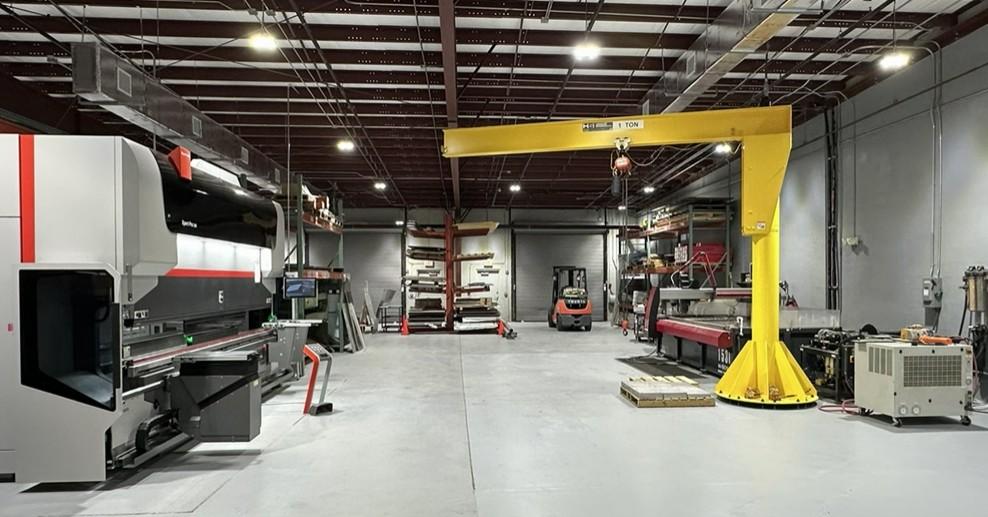A press brake and a large yellow overhead crane sit on a factory floor.